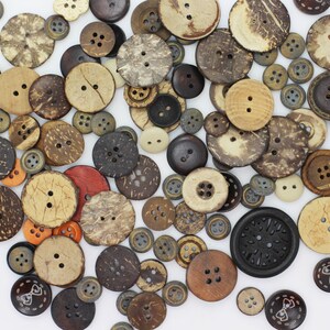 May include: A collection of brown, black, and natural coconut shell buttons with various patterns and designs. The buttons are scattered on a white background.