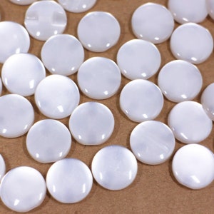 May include: A collection of white, round, smooth, and shiny buttons. The buttons are made of a pearlescent material and have a slightly iridescent sheen.