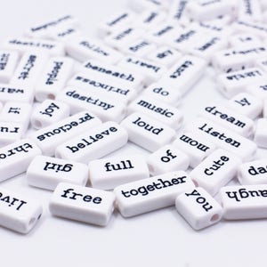 May include: White rectangular beads with black lettering spelling out words like "love", "dream", "music", "joy", "believe", "together", "free", "full", "cute", "dad", "listen", "wow", "laugh", and "run".