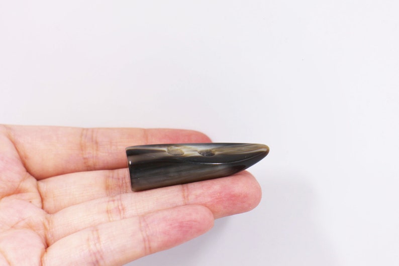 May include: A dark brown and black horn button with a pointed tip. The button is smooth and has a natural, organic look.