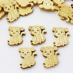 May include: A group of wooden monkey-shaped buttons, some are stacked on top of each other, while others are scattered on a white surface. The buttons are unpainted and have a natural wood colour.