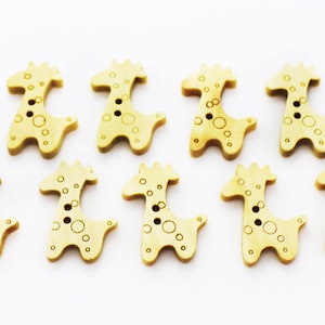 May include: Ten wooden buttons shaped like giraffes with brown spots. The buttons are light brown and have two holes.