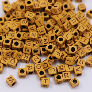 May include: A large pile of yellow letter beads with brown lettering. The beads are cube shaped and have a hole in the center.
