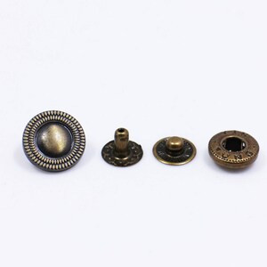 May include: Four antique gold-toned metal snap buttons. The buttons are round with a raised centre and a decorative border.