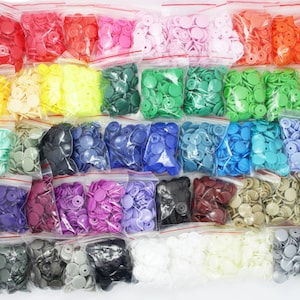 May include: Assortment of plastic snap buttons in various colours, packaged in individual clear plastic bags. The buttons are arranged in rows and columns, creating a colourful and organised display.