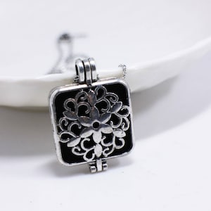 May include: Silver locket necklace with a black enamel square pendant featuring a detailed floral design.