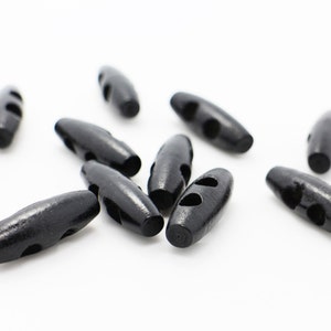 Peut inclure: Un groupe de boutons à bascule en bois noir avec deux trous chacun. Les boutons sont éparpillés sur une surface blanche.