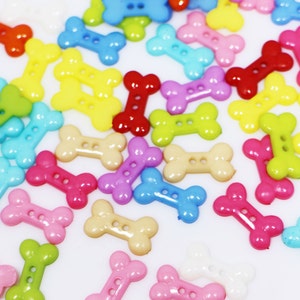 May include: A collection of colorful plastic bone-shaped buttons. The buttons are in various colors, including red, yellow, blue, green, pink, and purple.