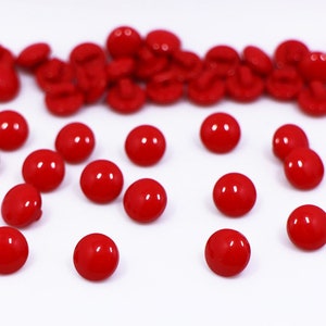 May include: A group of red plastic buttons scattered on a white surface. Some buttons are arranged in a line, while others are scattered randomly.