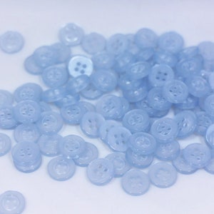 May include: A large pile of light blue plastic buttons. The buttons are round and have four holes.