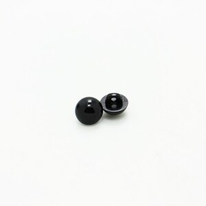 May include: Two black plastic buttons with a flat back and a round, raised front.