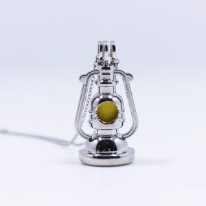 May include: A silver lantern charm necklace with a yellow glass insert. The lantern has a detailed design and is a popular choice for jewelry.