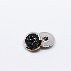May include: Two gold-toned buttons with a black rose design. The button on the left has a raised rose design, while the button on the right is plain.