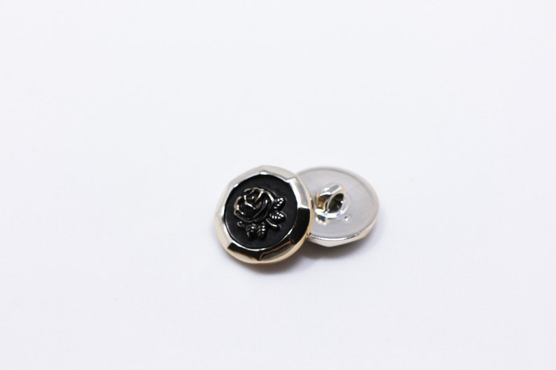May include: Two gold-toned buttons with a black rose design. The button on the left has a raised rose design, while the button on the right is plain.