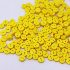 May include: A large pile of bright yellow plastic buttons with two holes each.