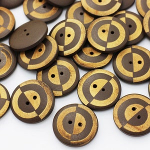 May include: A collection of brown wooden buttons with a gold concentric circle design. The buttons have two holes.