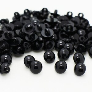 May include: A large pile of black plastic buttons with a shiny finish. Some buttons are laying flat, while others are standing upright.