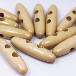 Könnte beinhalten: Eine Gruppe von 12 natürlichen Holz-Toggle-Knöpfen mit jeweils zwei Löchern. Die Knöpfe sind oval geformt und haben eine hellbraune Farbe.