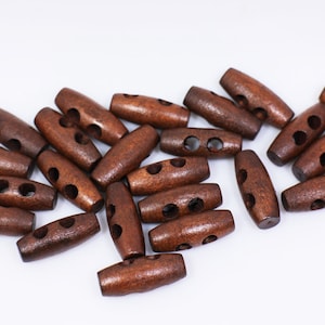 Könnte beinhalten: Ein Haufen brauner Holz-Toggle-Knöpfe mit jeweils zwei Löchern. Die Knöpfe sind oval geformt und haben eine glatte, polierte Oberfläche.