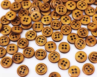 May include: A collection of brown wooden buttons with four holes each. The buttons are scattered on a white surface.