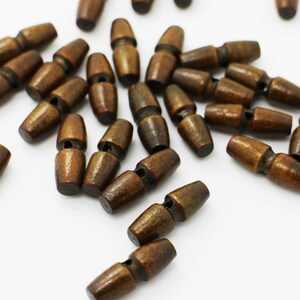 May include: A collection of brown wooden toggle buttons. The buttons are oval shaped and have a hole in the center. They are scattered on a white surface.