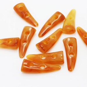 May include: A group of ten amber-colored plastic horn buttons with two holes each. The buttons are arranged in a star shape on a white background.