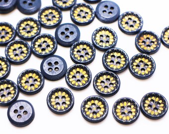 May include: A collection of blue and yellow wooden buttons with a floral design. The buttons are arranged in a line on a white background.
