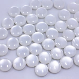May include: A group of white round cabochon gems, with a pearlescent finish, scattered on a white surface.