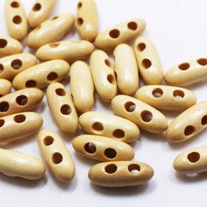 Könnte beinhalten: Ein Haufen naturfarbener Holz-Toggle-Knöpfe mit jeweils zwei Löchern. Die Knöpfe sind oval geformt und haben eine glatte, unbehandelte Oberfläche.