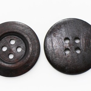 May include: Two dark brown wooden buttons with four holes each. The buttons are round and have a smooth surface.