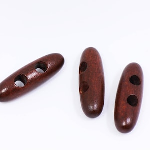 May include: Three brown wooden toggle buttons, each with two holes. The buttons are oval shaped and have a smooth, polished finish.