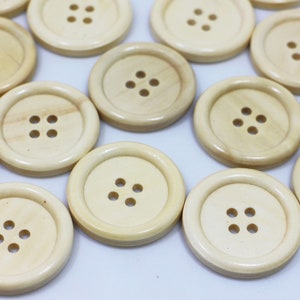 May include: A collection of 12 natural wood buttons, each with four holes. The buttons are a light beige colour and have a smooth, polished finish.