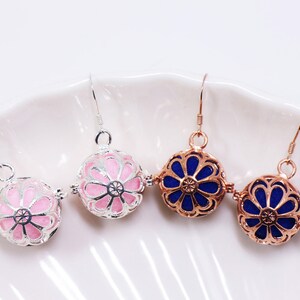 May include: Three pairs of silver, rose gold, and gold tone earrings with a flower design. The earrings have a pink, blue, and blue enamel finish.