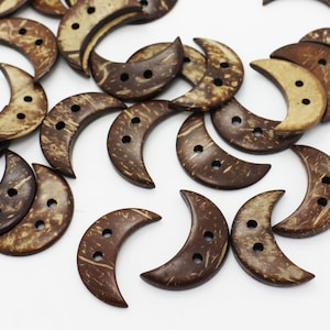 May include: A selection of crescent-shaped buttons crafted from natural coconut shells. Each button features two sewing holes and displays a mix of light and dark brown hues. The buttons are scattered on a white surface.
