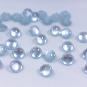 May include: A collection of light blue round glass beads, scattered on a white surface.