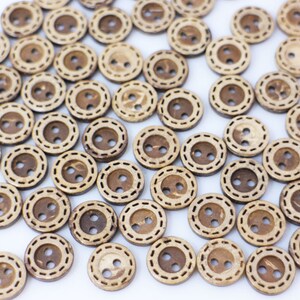 May include: A collection of brown coconut shell buttons with a double stitched design. The buttons are round and have two holes.