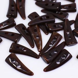 May include: A group of brown plastic buttons shaped like horns. The buttons have two holes each.