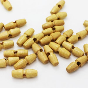 以下が含まれることがあります： 薄い茶色の木製トグルボタンの山。ボタンは白い表面にランダムなパターンで配置されています。