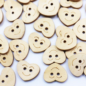 Könnte beinhalten: Eine Sammlung von herzförmigen Holzknöpfen mit einem Smiley-Gesicht. Die Knöpfe sind hellbraun und haben zwei Löcher zum Nähen.