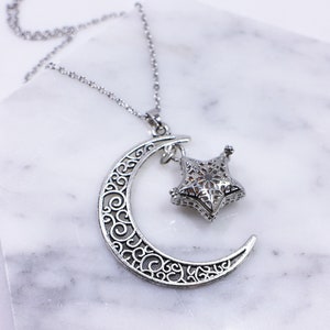 May include: A silver necklace featuring a crescent moon and star pendant. Both the moon and star are intricately designed with filigree details.