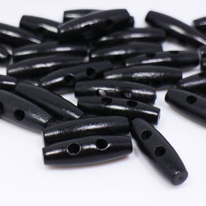 Könnte beinhalten: Eine Gruppe schwarzer Holz-Toggle-Knöpfe mit jeweils zwei Löchern. Die Knöpfe sind oval geformt und haben eine glatte, polierte Oberfläche.