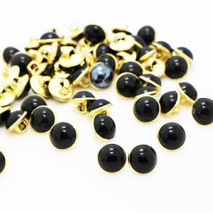 May include: A pile of black and gold buttons. The buttons are round and have a shiny finish.