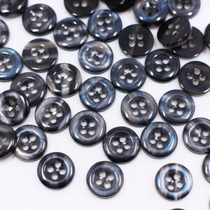 May include: A collection of black and silver buttons with a swirl pattern. The buttons are arranged in a random pattern on a white surface.