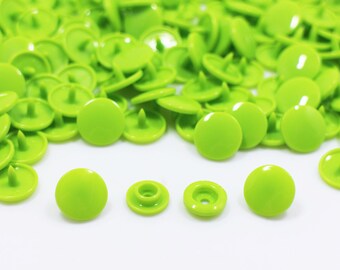 May include: A large pile of lime green plastic snap buttons. The buttons are round and have a small post on the back. There are also two separate snap buttons in the foreground.