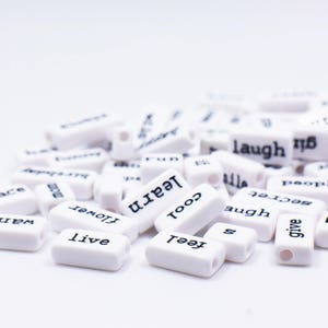 May include: White rectangular tiles with black lettering spelling out words like "hug", "feel", "give", "thing", "wild", "live", "believe", "want", "peace", "flower", "learn", "cool", "augh", "secret", "laugh", "people", and "family".