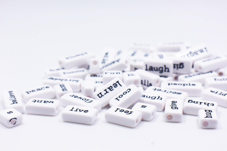 May include: White rectangular tiles with black lettering spelling out words like "hug", "feel", "give", "thing", "wild", "live", "believe", "want", "peace", "flower", "learn", "cool", "augh", "secret", "laugh", "people", and "family".