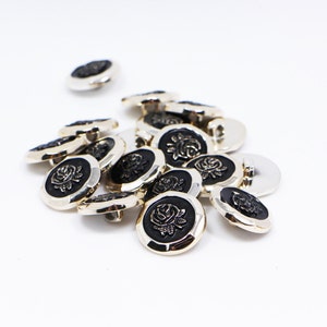 May include: A group of silver-toned buttons with black centers featuring a raised rose design.