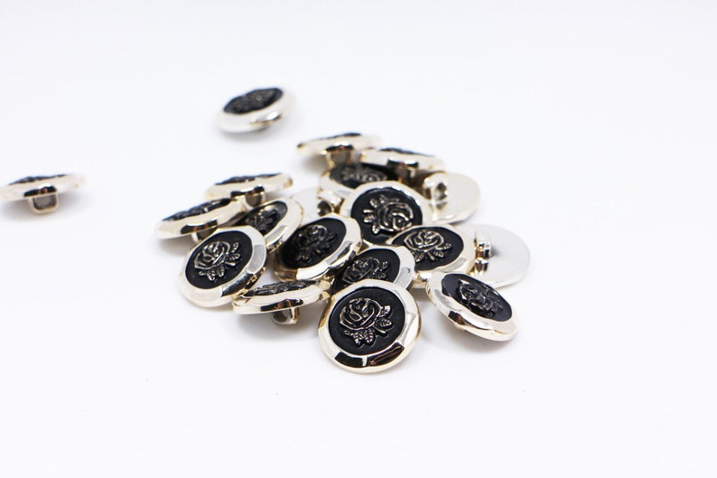 May include: A group of silver-toned buttons with black centers featuring a raised rose design.