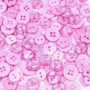 May include: A large assortment of pink buttons in various shapes and sizes. Some buttons are solid pink, while others have a clear, translucent finish with a floral design.