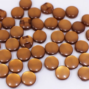 May include: A large group of round, brown buttons with a shiny finish. The buttons are scattered on a white surface.